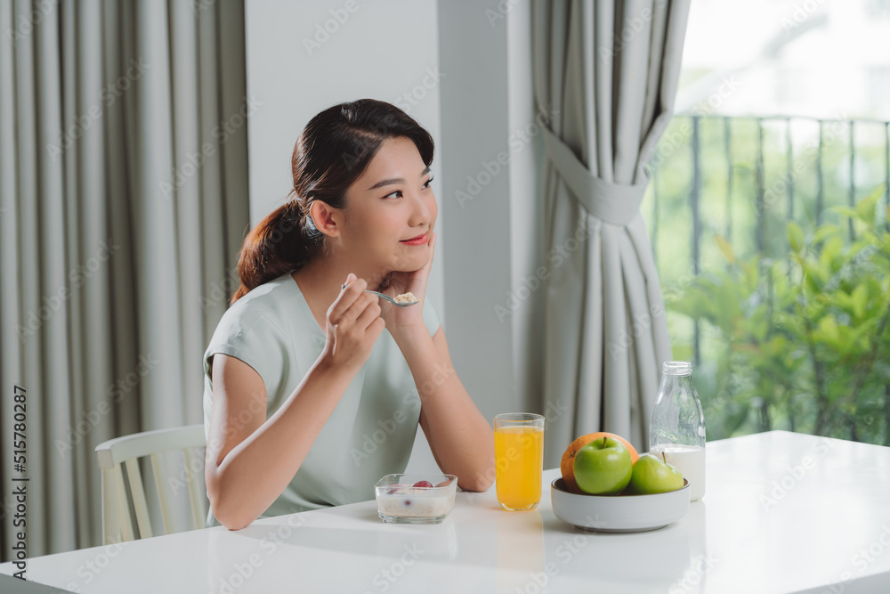 Thoughtful young woman in bathrobe eating breakfast in kitchen