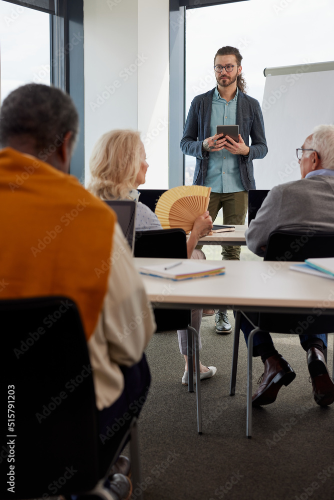 Young hipster teacher is educating a multicultural group of senior people about social media in the classroom.