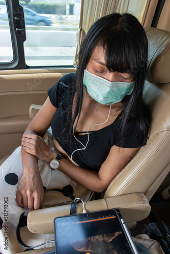 A woman with a protective mask travels in a minivan and watches a movie on a portable device