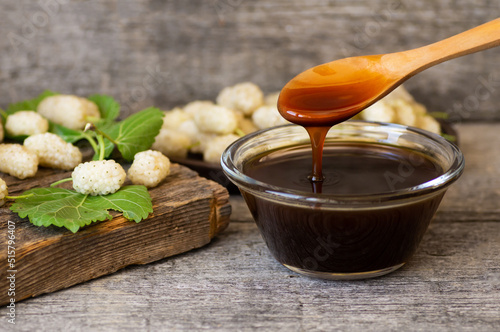 White mulberry molasses in glass bowl and wooden spoon with fresh mulberries, healthy food