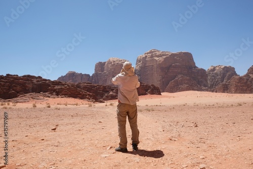 Silhouette of man in tropic clothes, who is standing and taking picture of amazing Martian scenery of Wadi Rum desert with red sand. Jordan