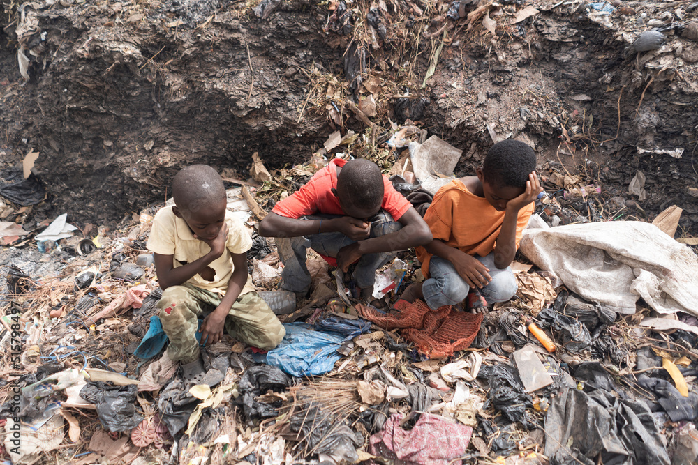 Three little African boys sitting on a landfill suffering from breathing problems, burning eyes, headaches, sore throats and the unbearable smell; Concept of child exploitation and health risks