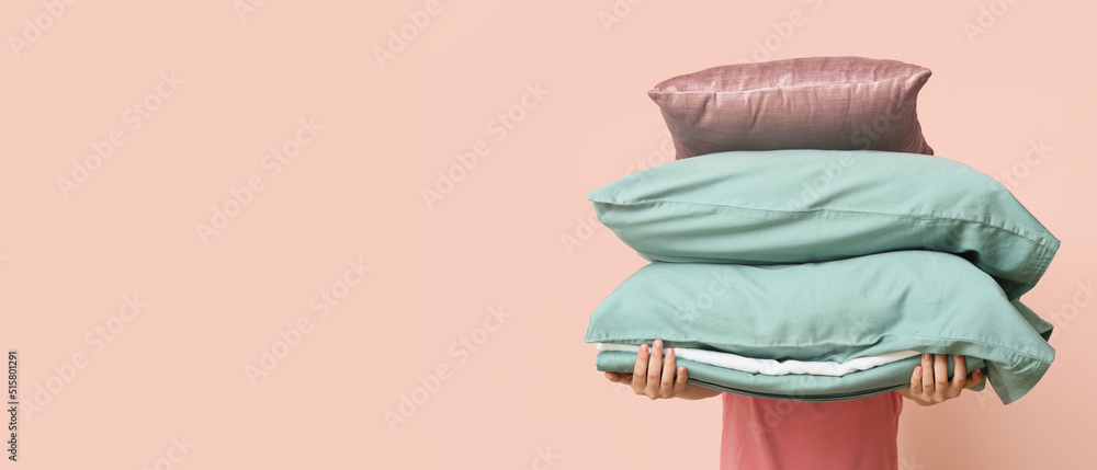 Woman holding soft pillows and bedsheets on pink background with space for text Woman holding soft pillows and bedsheets on pink background with space for text