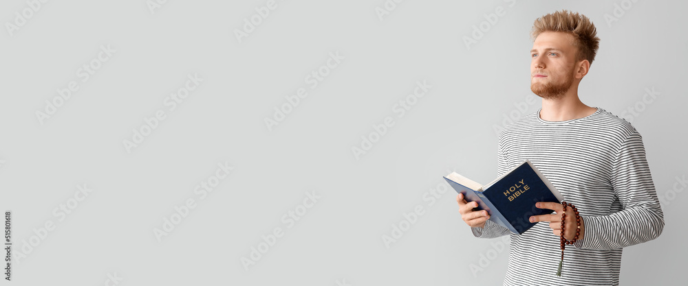 Religious young man with Bible praying to God on light background with space for text Religious young man with Bible praying to God on light background with space for text