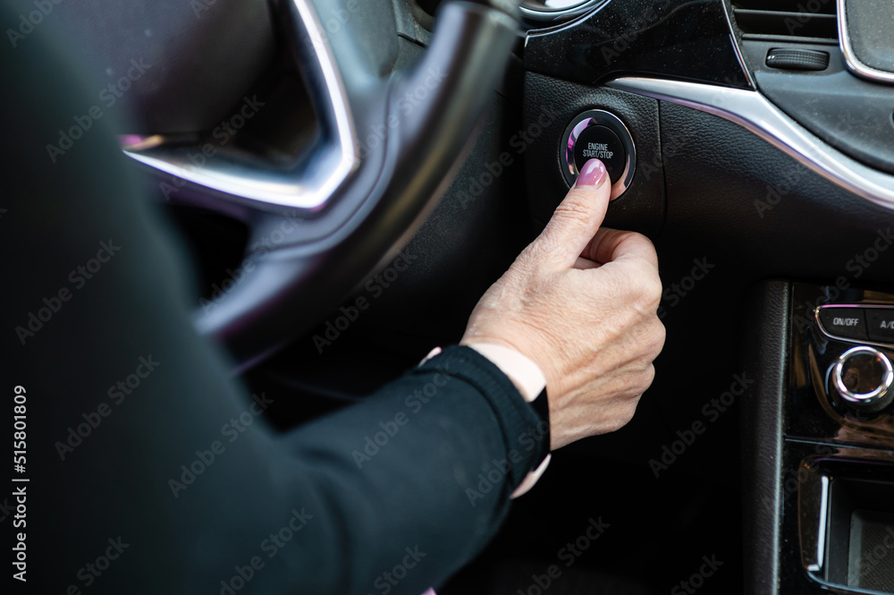Woman hand pushing on car engine start-stop button. Modern car interior, closeup