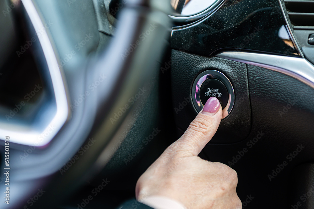 Woman hand pushing on car engine start-stop button. Modern car interior, closeup