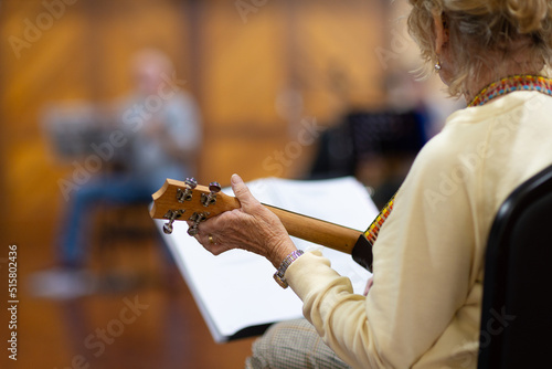 detail of senior lady playing ukulele with blurred musician in background