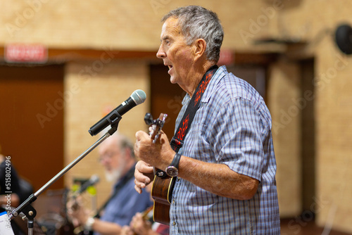 man playing ukulele and singing into microphone photo