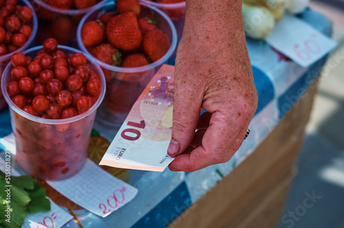 Selling berries at the farmers' market. Cherries and strawberries in plastic glasses. Elderly woman's hand holding a 10 euro banknote. Organic food. Trade concept. Close up. Selective focus. photo