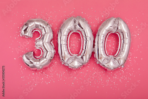 From above of silver shiny balloons demonstrating number 300 three hundred pink background with scattered glitter