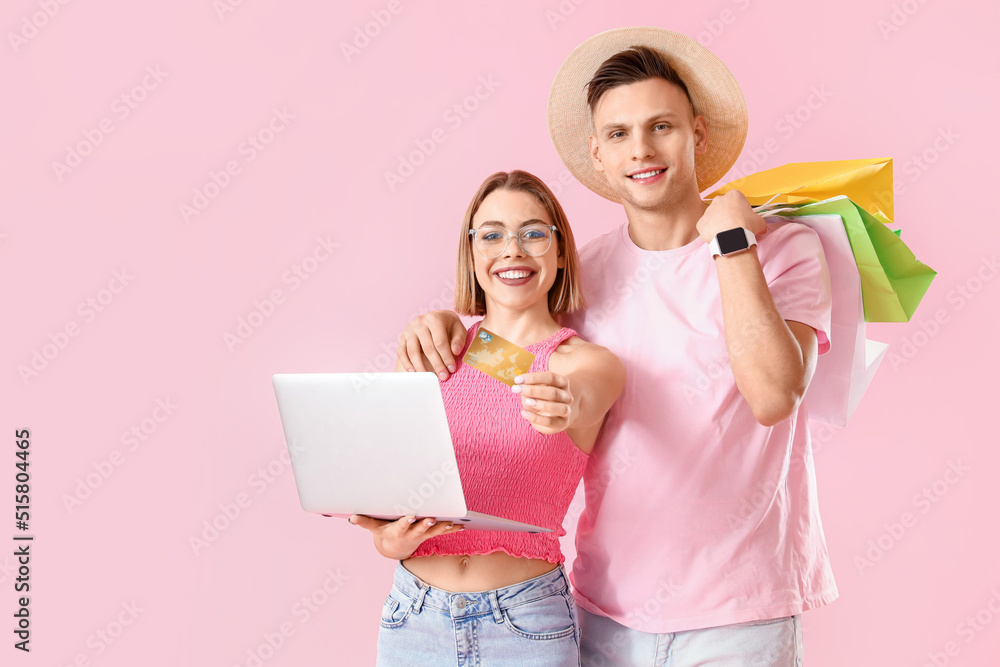 Young couple with laptop, credit card and shopping bags on pink background. Online shopping Young couple with laptop, credit card and shopping bags on pink background. Online shopping