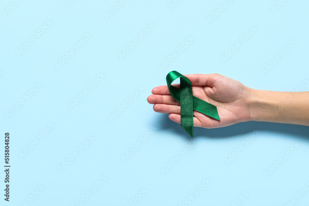 Hand with green ribbon on light blue background. Liver cancer concept Hand with green ribbon on light blue background. Liver cancer concept
