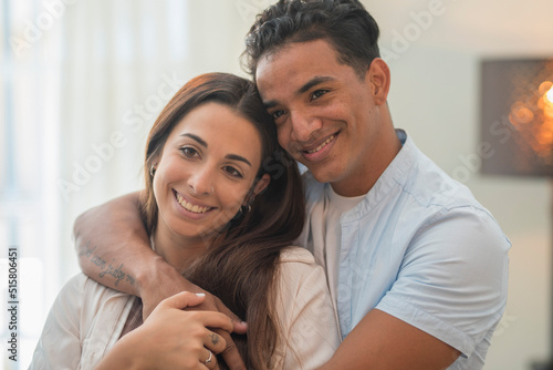 Concept of young interracial couple in love and relationship. Boy hug and protect girlfriend at home. Life and future together man and woman. New apartment happiness satisfaction portrait. Smile