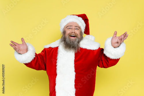 joyful and chubby santa claus showing greeting gesture isolated on yellow.