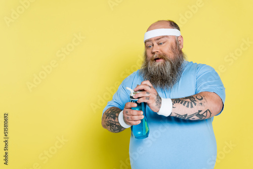 thirsty overweight man with beard opening sports bottle isolated on yellow.