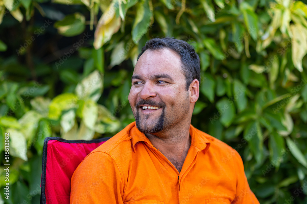 man wearing orange looking away outside with green leafy background man wearing orange looking away outside with green leafy background