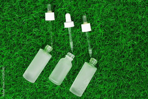 Serum for the face. A jar with a pipette on green grass. Summer skin care. Serum on green grass.