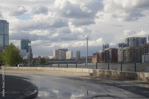 Full-color horizontal photo. An urban landscape with a pond and a stormy sky. Cloud cover has a complex structure.