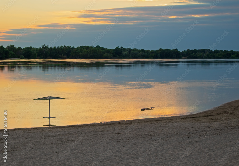 Empty beach in the evening. Bank of the river (lake). Sunset and calm water surface