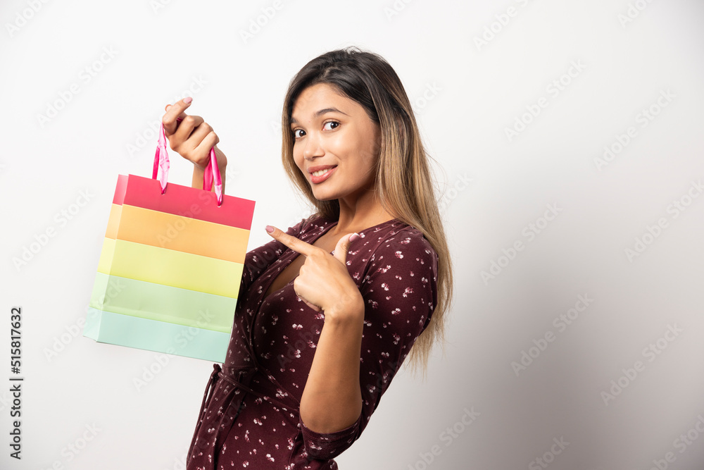 Young woman pointing at a small shop bag on white background Young woman pointing at a small shop bag on white background