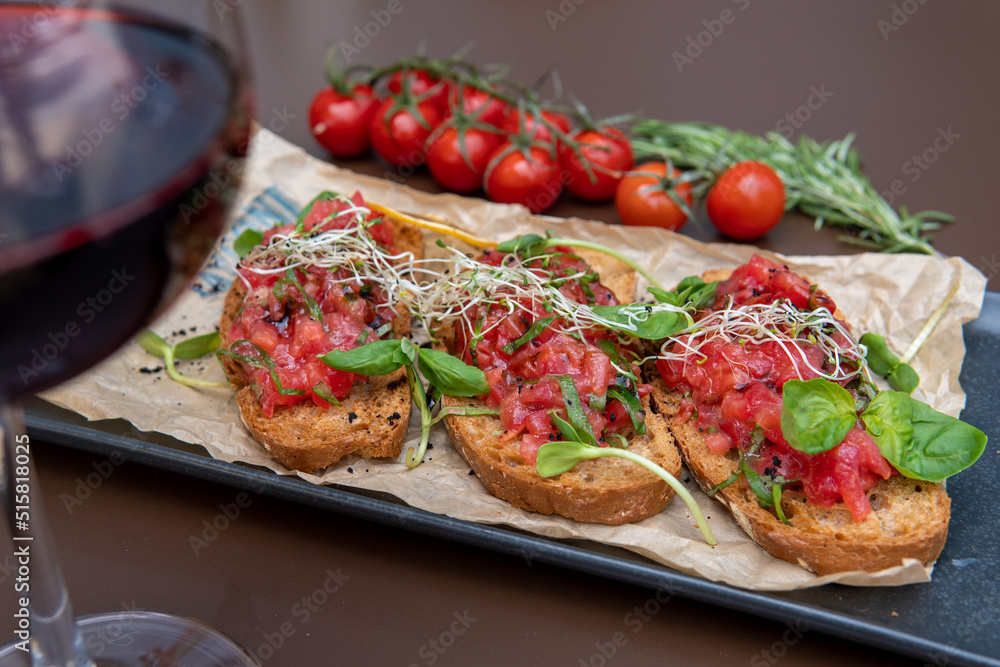 a bruschetta with tomatoes on a dark table, a glass of red wine