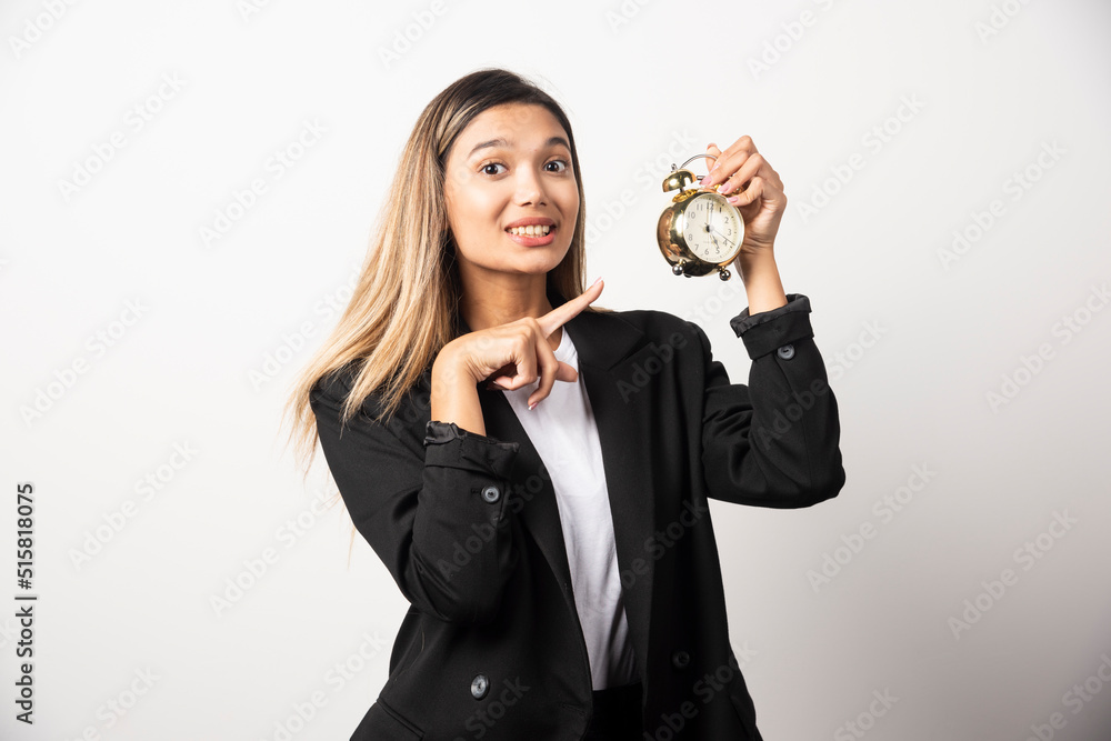 Business woman pointing at an alarm clock on white background Business woman pointing at an alarm clock on white background