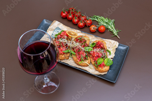 a bruschetta with tomatoes on a dark table, a glass of red wine