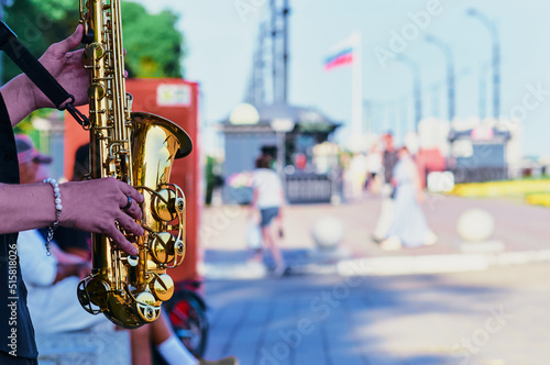 Print op canvas Street musician saxophonist plays jazz on the saxophone on the city embankment at the weekend