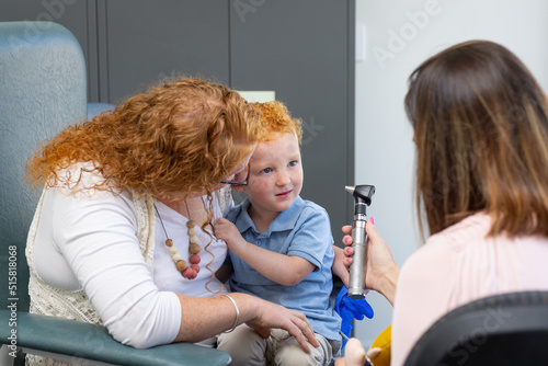 doctor showing otoscope to little boy sitting on mother's lap photo