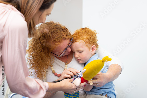 little boy sitting on mum's lap with health professional photo