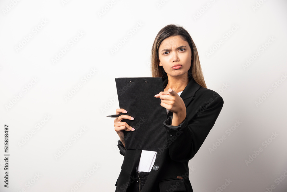 Young business woman holding clipboard and pointing at camera Young business woman holding clipboard and pointing at camera