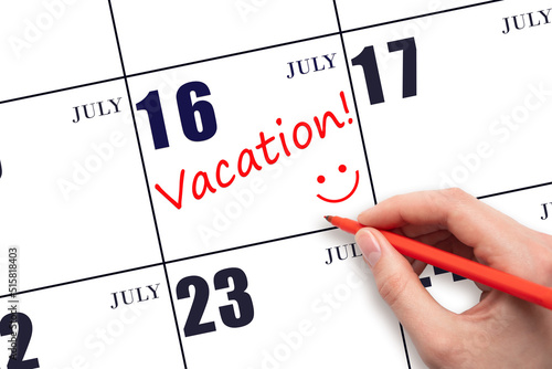 A hand writing a VACATION text and drawing a smiling face on a calendar date 16July. Vacation planning concept. photo