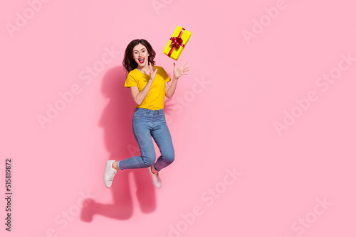 Full length photo of impressed young brunette lady jump with present wear t-shirt jeans sneakers isolated on pink background