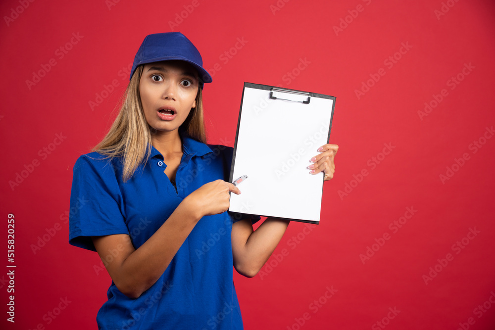 Young woman in blue uniform pointing at clipboard with pencil Young woman in blue uniform pointing at clipboard with pencil