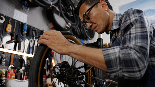 Asian senior man owner repairing and checking wheels and gears of bicycle while standing in bicycle shop