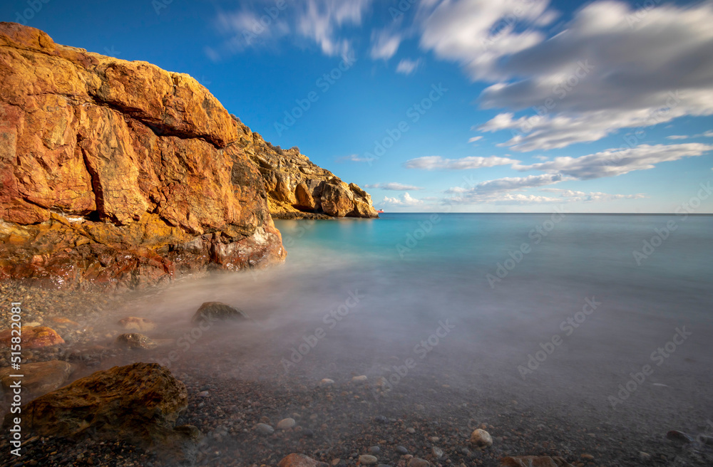 Scenic landscape of a small beach on the coast of Cartagena, Spain, taken with long exposure in which the colors of the rocks, the sea and the sky stand out