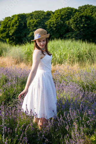 portrait of a beautiful sexy smiling woman  in straw hat and white dress walking in lavender field