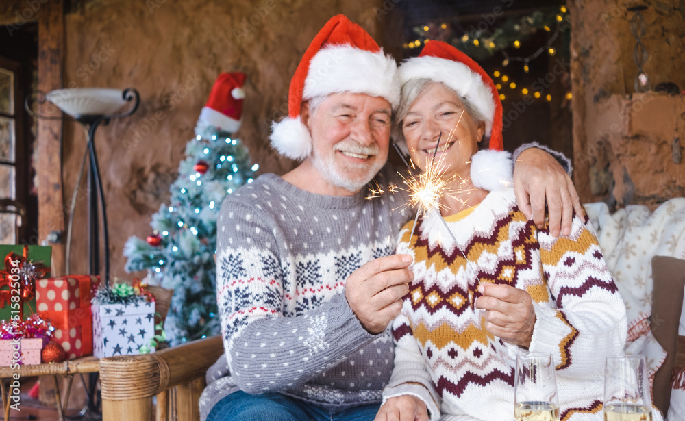 Defocused senior couple in Santa hats smiling and hugging at home at Christmas time with sparklers. Christmas Family Love concept. Focus on sparklers Defocused senior couple in Santa hats smiling and hugging at home at Christmas time with sparklers. Christmas Family Love concept. Focus on sparklers