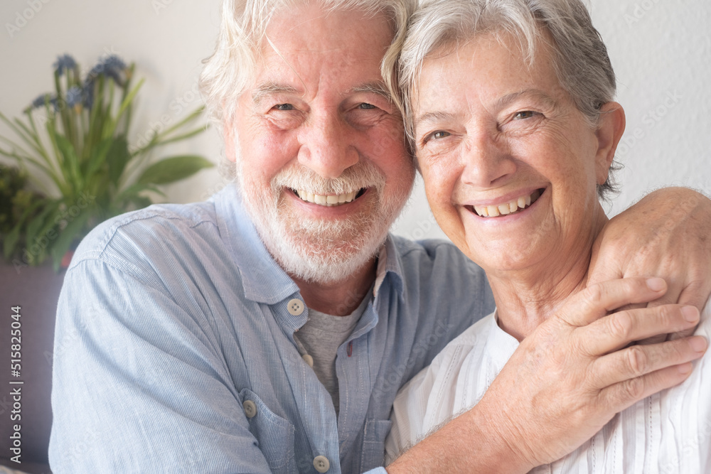 Beautiful caucasian senior couple hugging sitting at home on sofa. Serene elderly people enjoying retirement Beautiful caucasian senior couple hugging sitting at home on sofa. Serene elderly people enjoying retirement