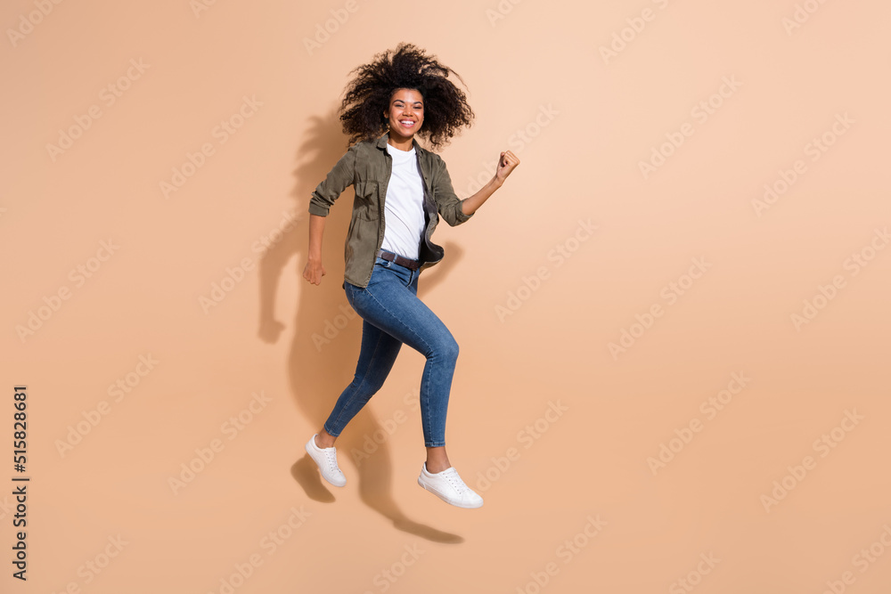Full length body size view of pretty cheerful thin sportive girl jumping running isolated over beige pastel color background Full length body size view of pretty cheerful thin sportive girl jumping running isolated over beige pastel color background