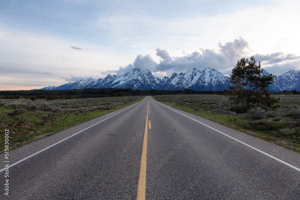 Scenic Road surrounded by Mountains and Trees in American Landscape. Spring Season. Grand Teton National Park. Wyoming, United States. Nature Background. Scenic Road surrounded by Mountains and Trees in American Landscape. Spring Season. Grand Teton National Park. Wyoming, United States. Nature Background.