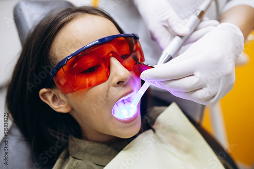 Girl whitening teeth at dentistry with special equipment