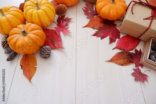 Autumn seasonal concept background. Autumn leaves, pumpkin and gift box on white wooden background. Thanks giving, Halloween and Autumn event decorative elements. 