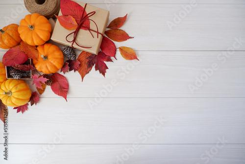 Autumn seasonal concept background. Autumn leaves  pumpkin and gift box on white wooden background. Thanks giving  Halloween and Autumn event decorative elements. 