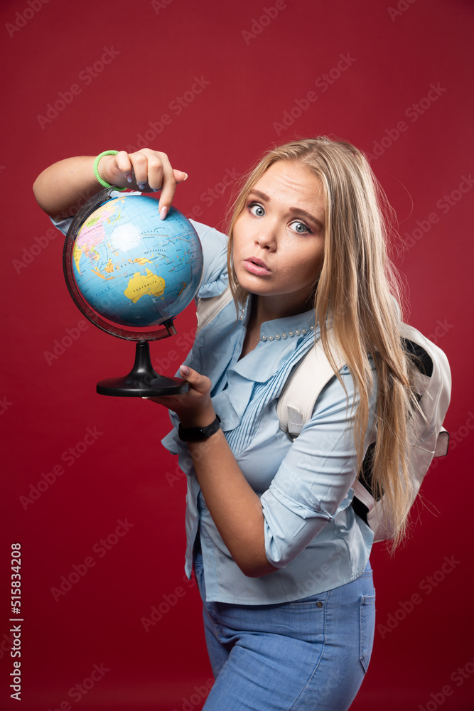 Blonde studentgirl holds a globe and looks surprized Blonde studentgirl holds a globe and looks surprized
