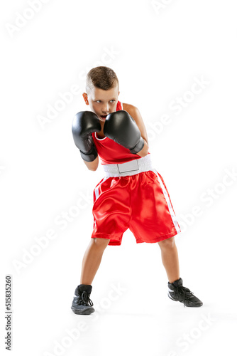 Portrait of active boy, beginner boxer in sports gloves and red uniform isolated on white background. Concept of sport, movement, studying, achievements, lifestyle. © master1305