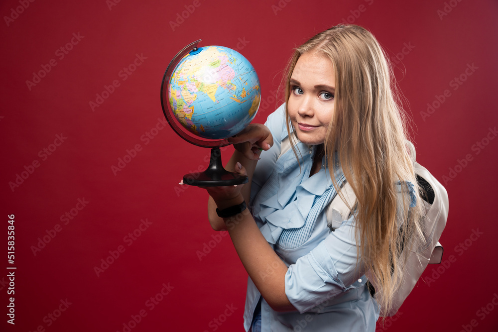 Blonde studentgirl holds a globe and looks positive Blonde studentgirl holds a globe and looks positive