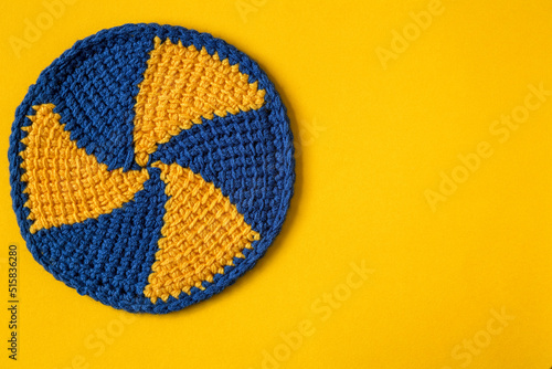 Round blue yellow cup coaster with spiral pattern on a yellow background. Crochet coaster with tunisian pattern. Copy space.
