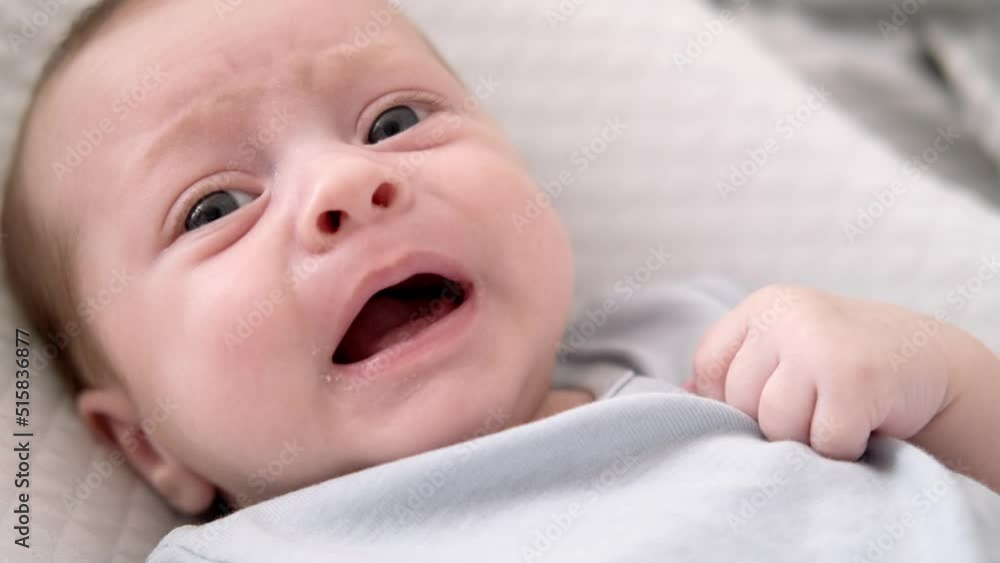Dissatisfied, crying, upset, sad Newborn baby boy lying in nursery cocoon with blue clothes on bed in bedroom at home, baby morning Dissatisfied, crying, upset, sad Newborn baby boy lying in nursery cocoon with blue clothes on bed in bedroom at home, baby morning