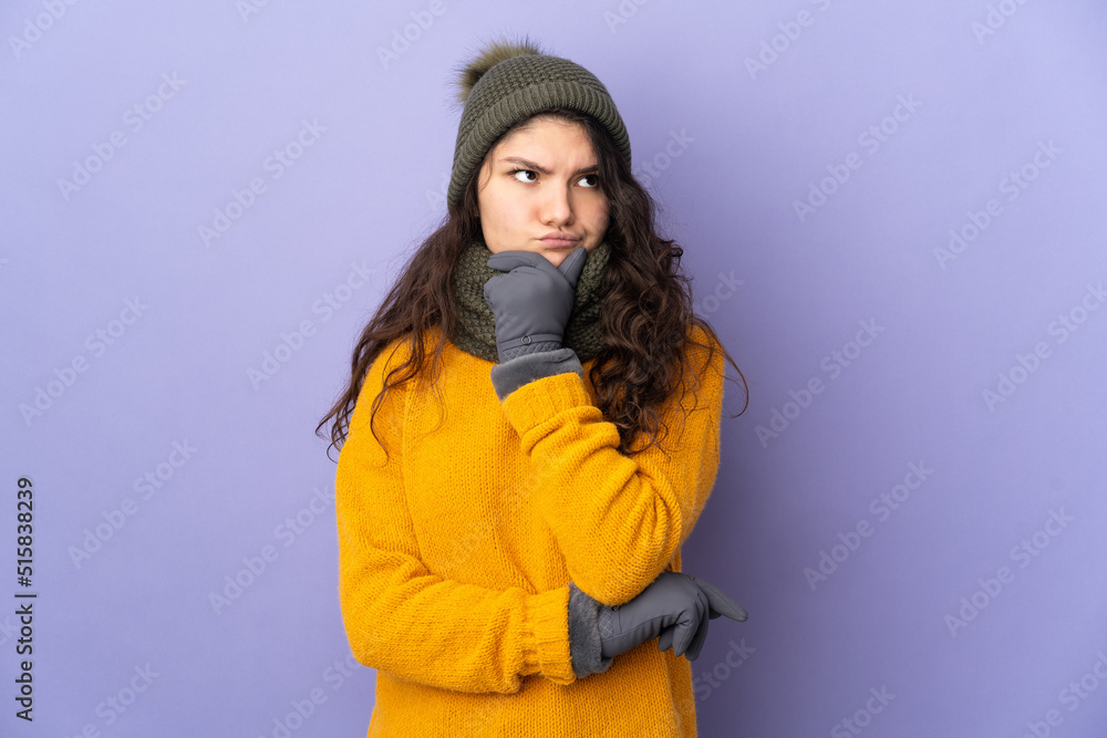 Teenager Russian girl with winter hat isolated on purple background having doubts Teenager Russian girl with winter hat isolated on purple background having doubts